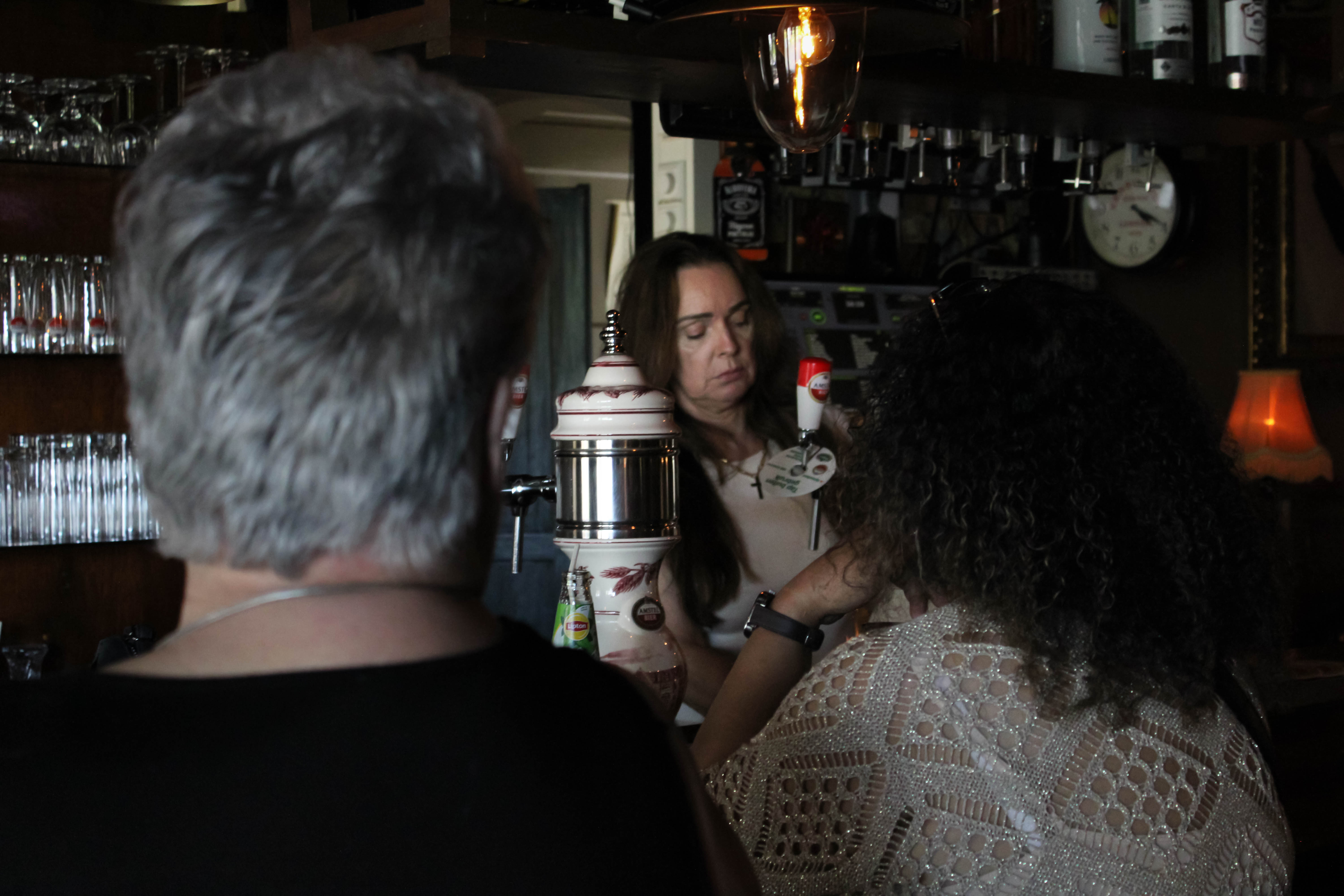 De eigenaresse achter de tap, gezien tussen twee gasten aan de bar
