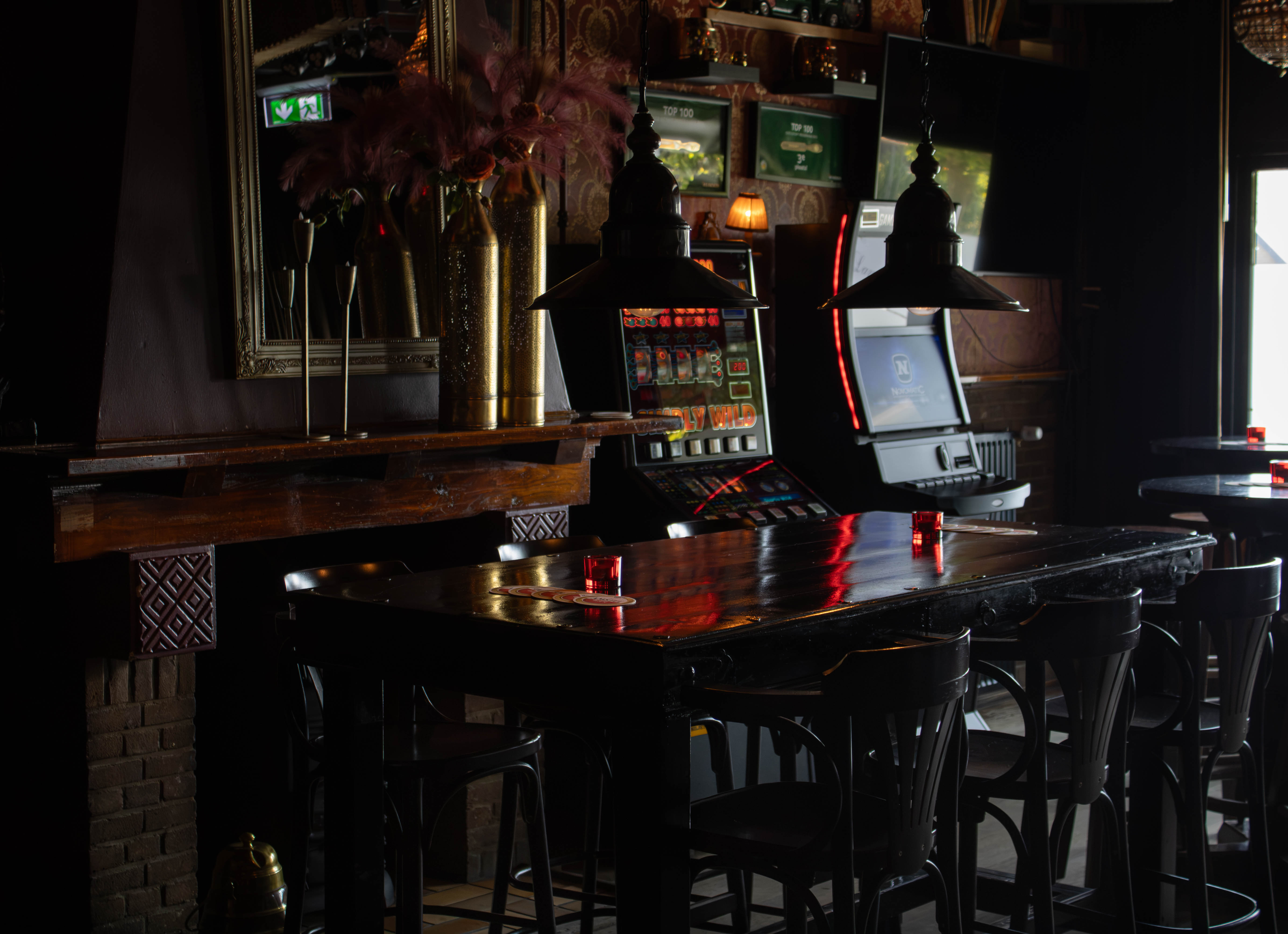 Een lege tafel met rode kaarsenhouders, hanglampen en speelautomaten in het café