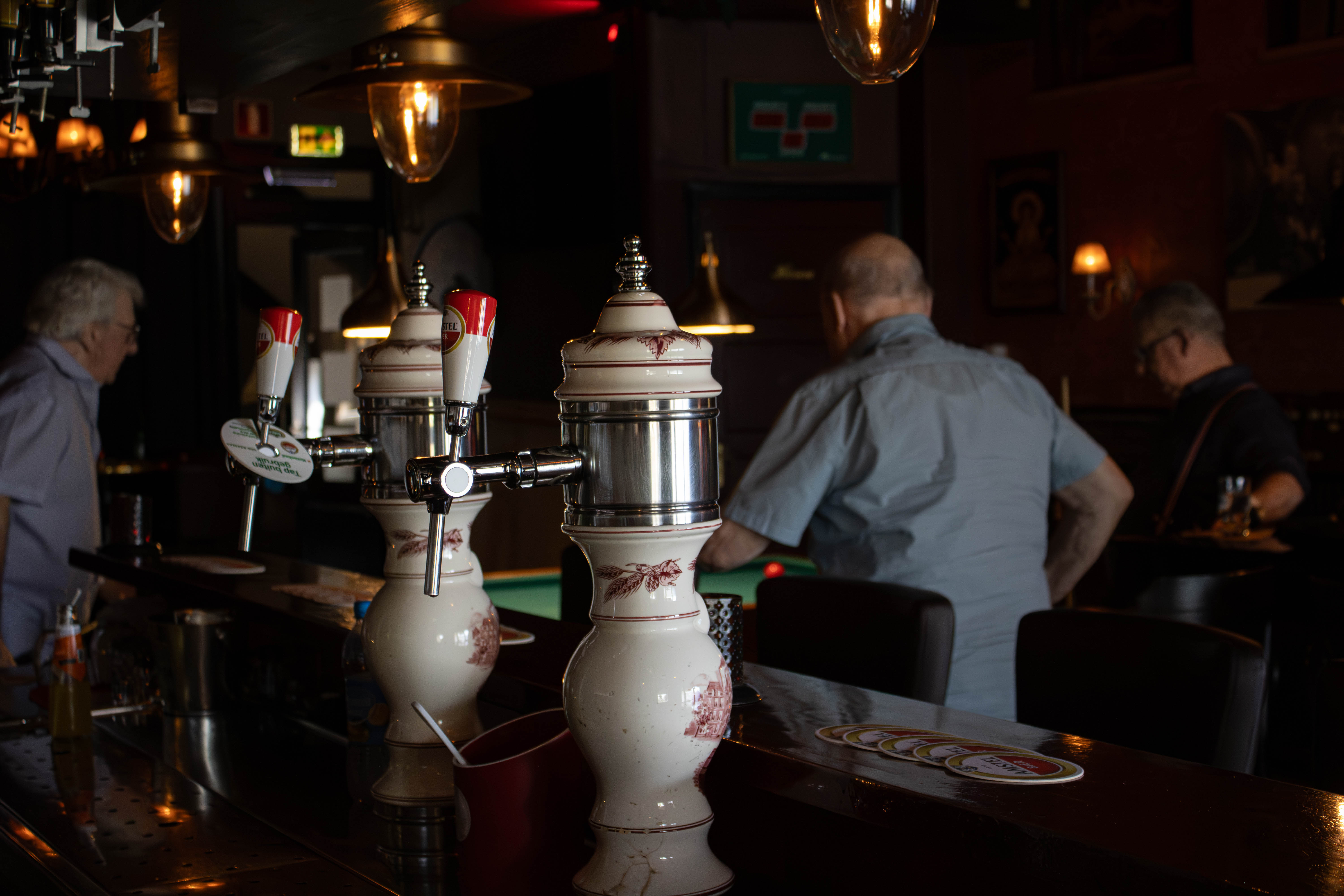 Porseleinen biertappen op de voorgrond, met biljarters op de achtergrond
