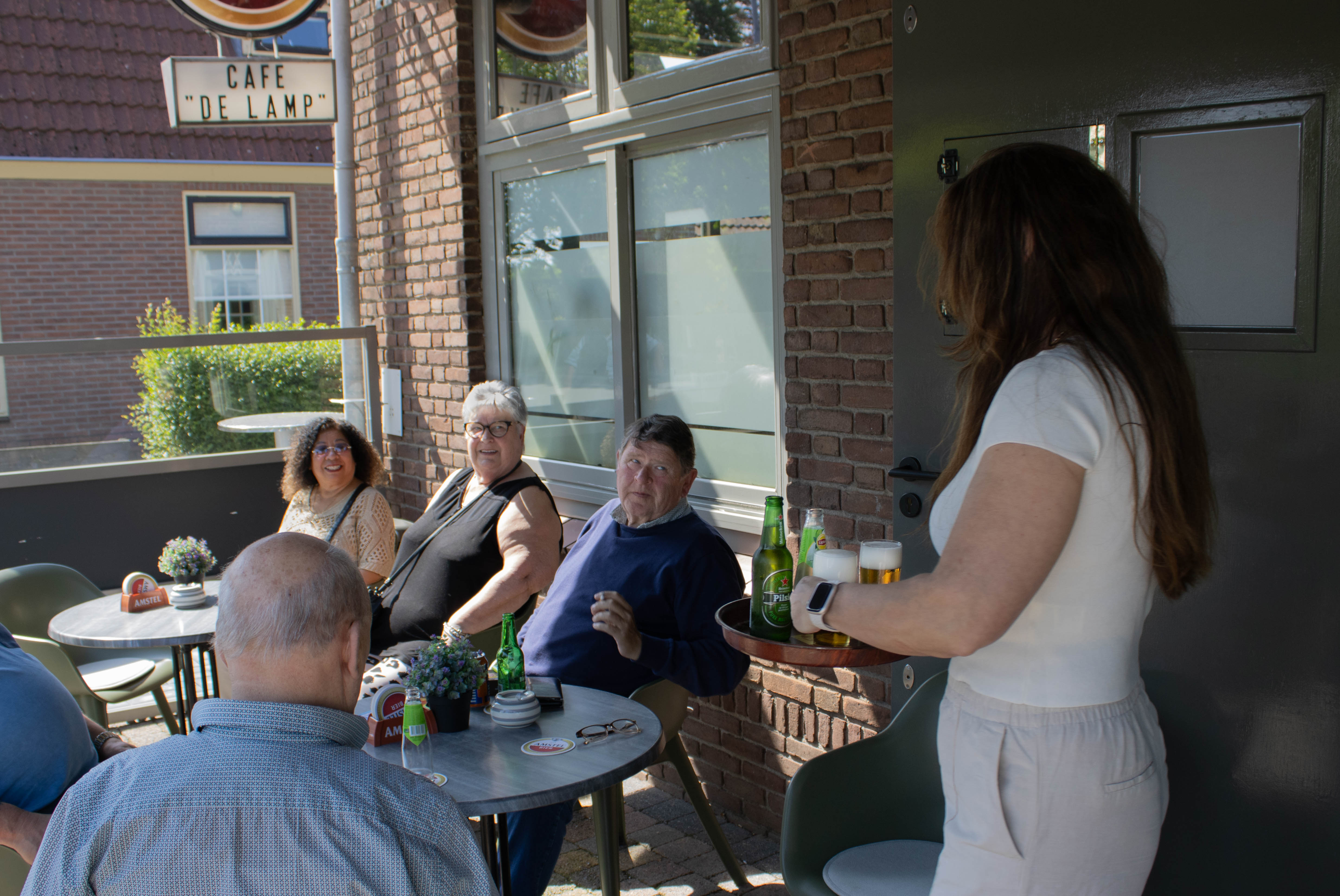 De eigenaresse brengt een dienblad met drankjes naar gasten op het terras